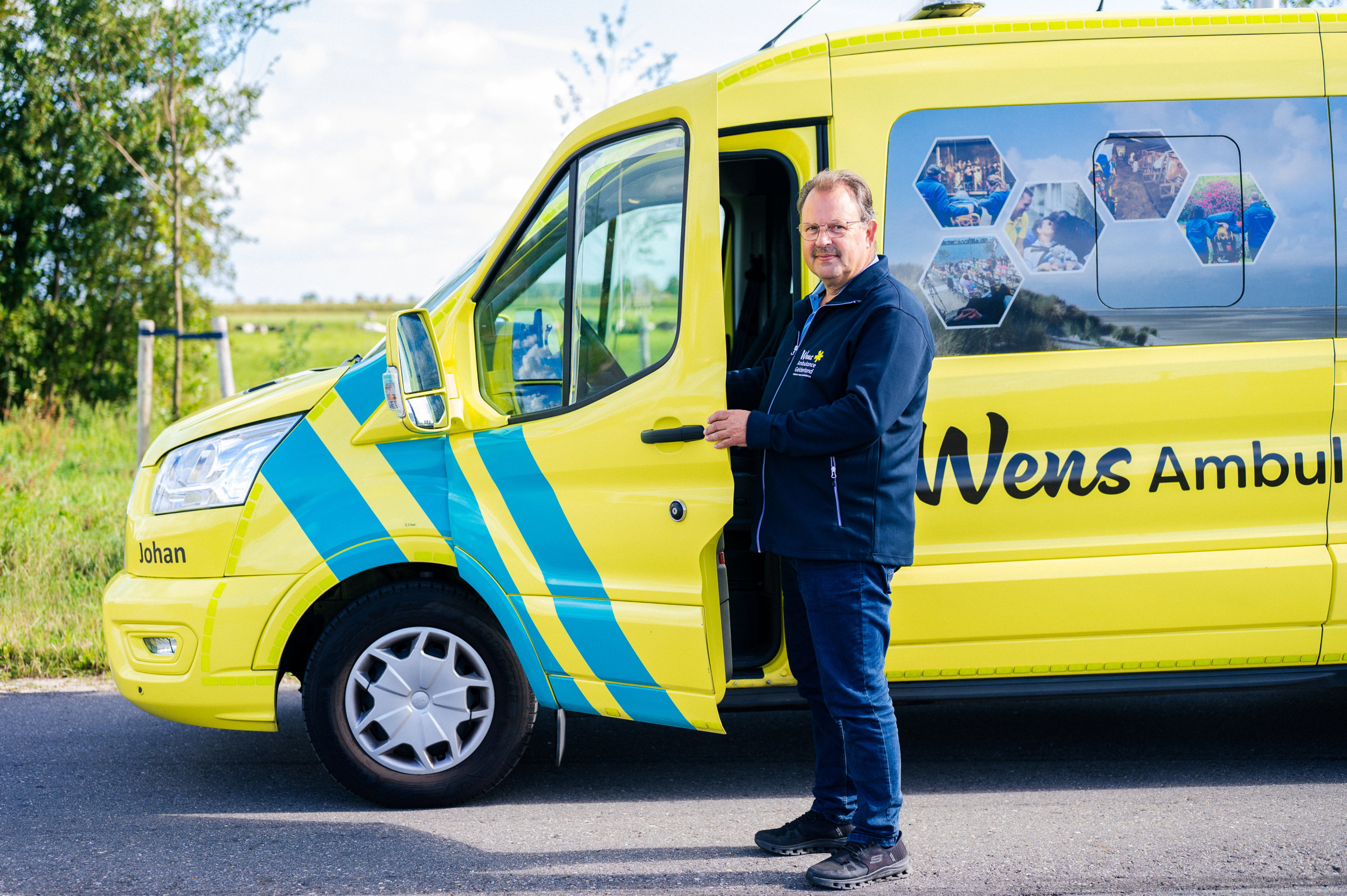 Een man in donkerblauwe kleding, bij een gele wensambulance.