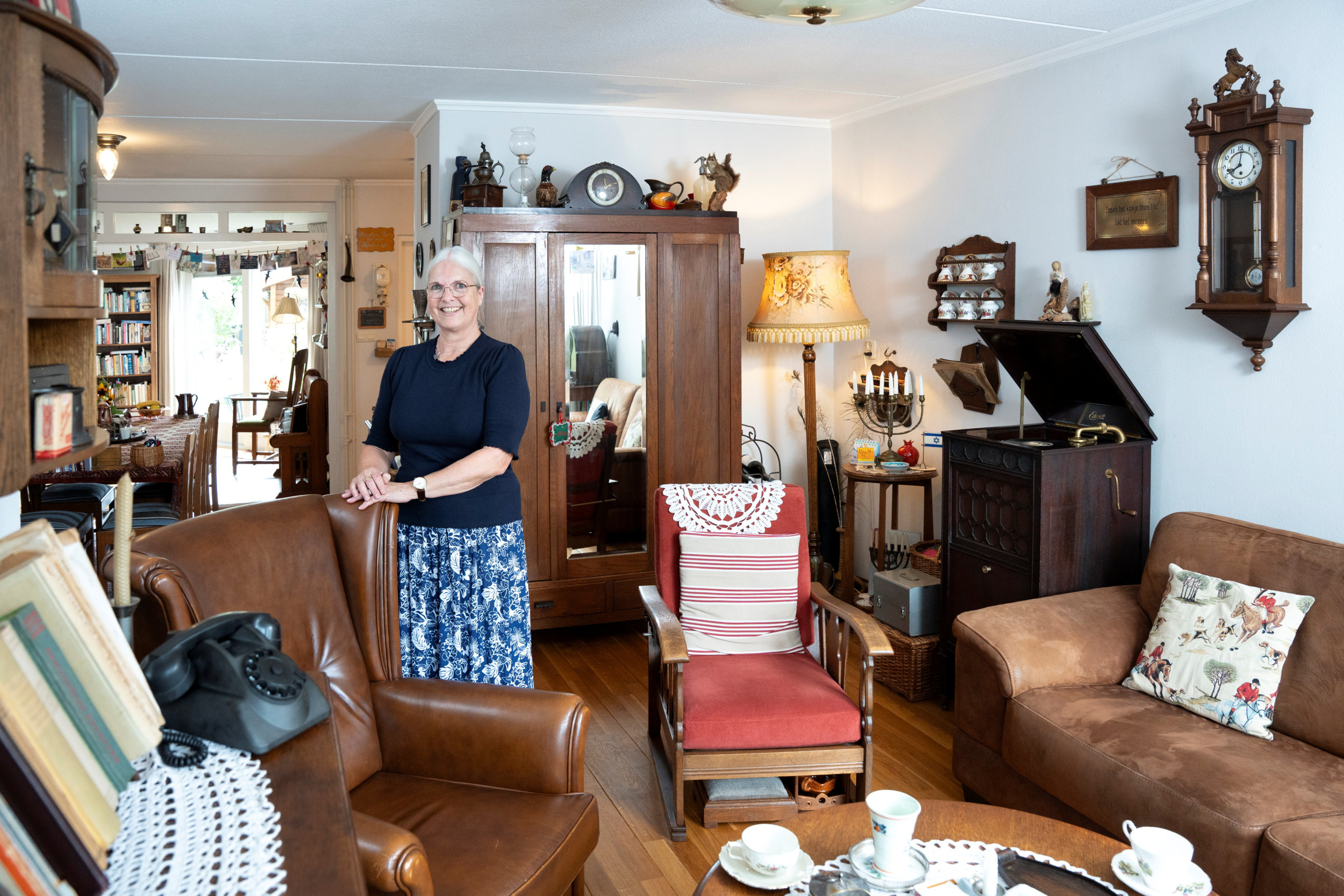 Oudere vrouw in een woonkamer vol met oude spulletjes. 