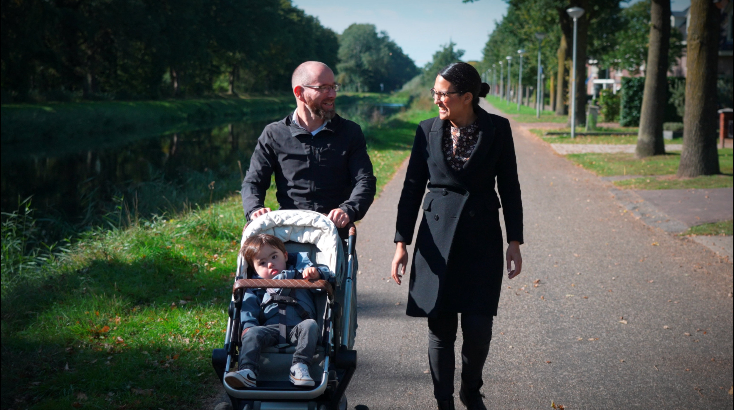 Vader en moeder met kindje in wandelwagen wandelen buiten. 