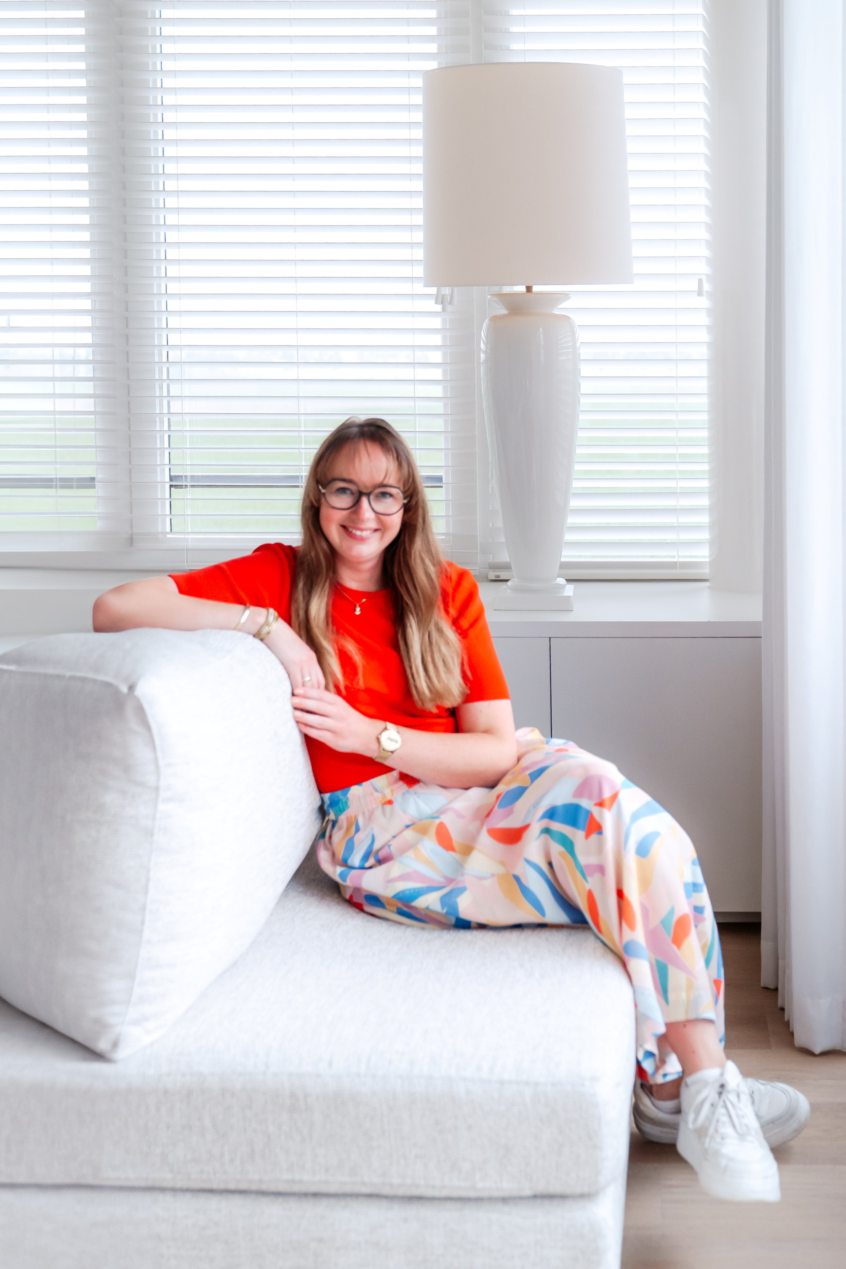 Jonge vrouw met lang haar, een bril en een rood shirt zittend op een bank