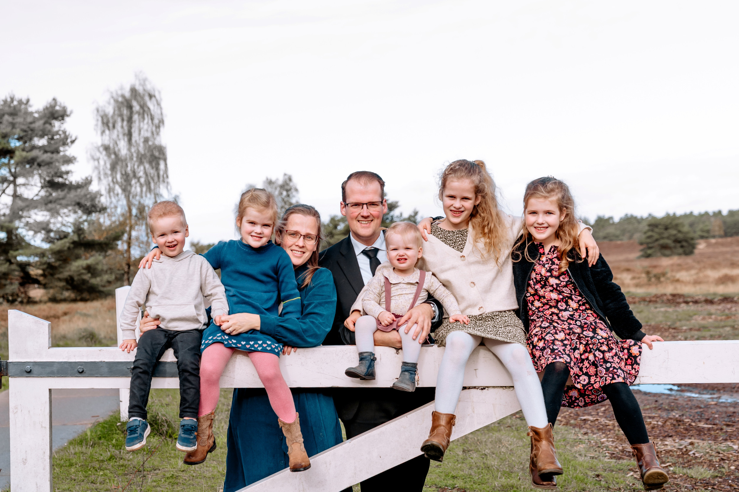 Echtpaar met vijf jonge kinderen achter een wit hek in de natuur.
