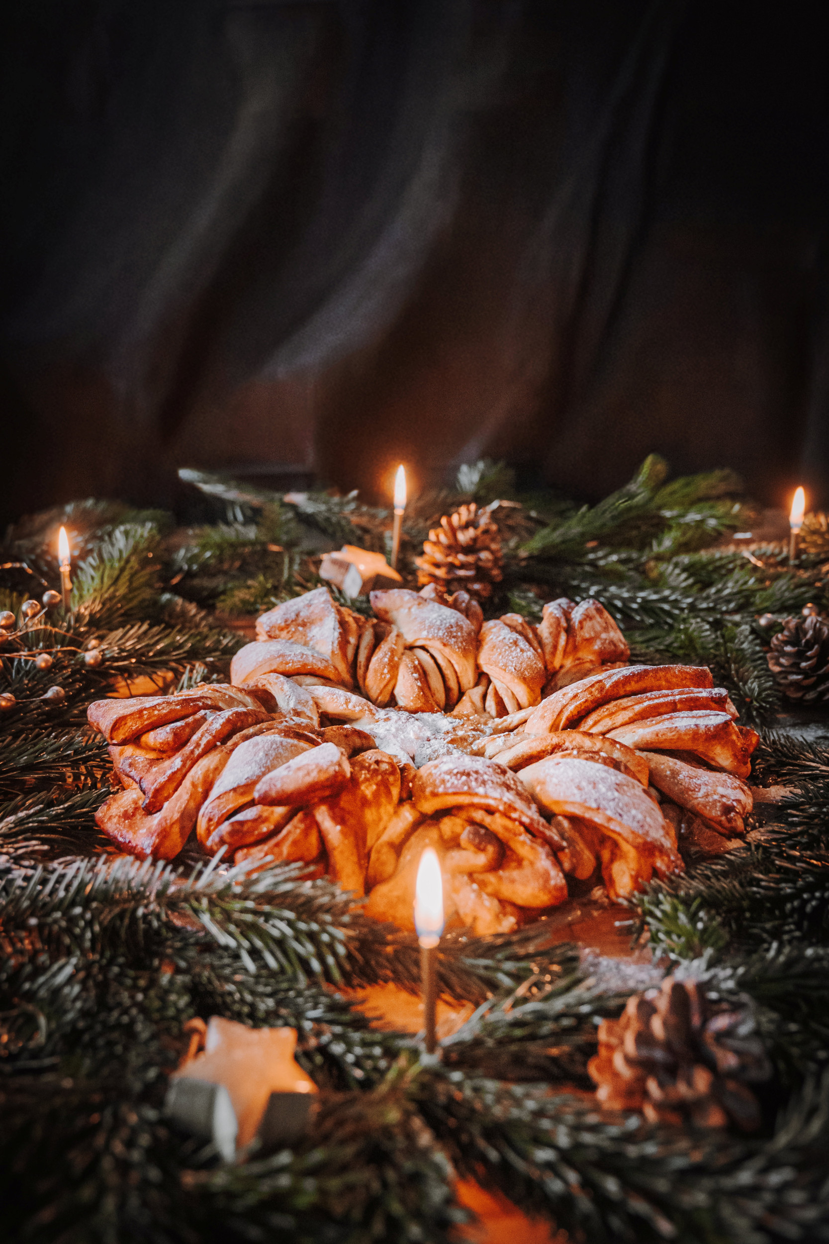 Een brood in de vorm van een kerstster. Daar omheen dennengroen en kaarsjes.
