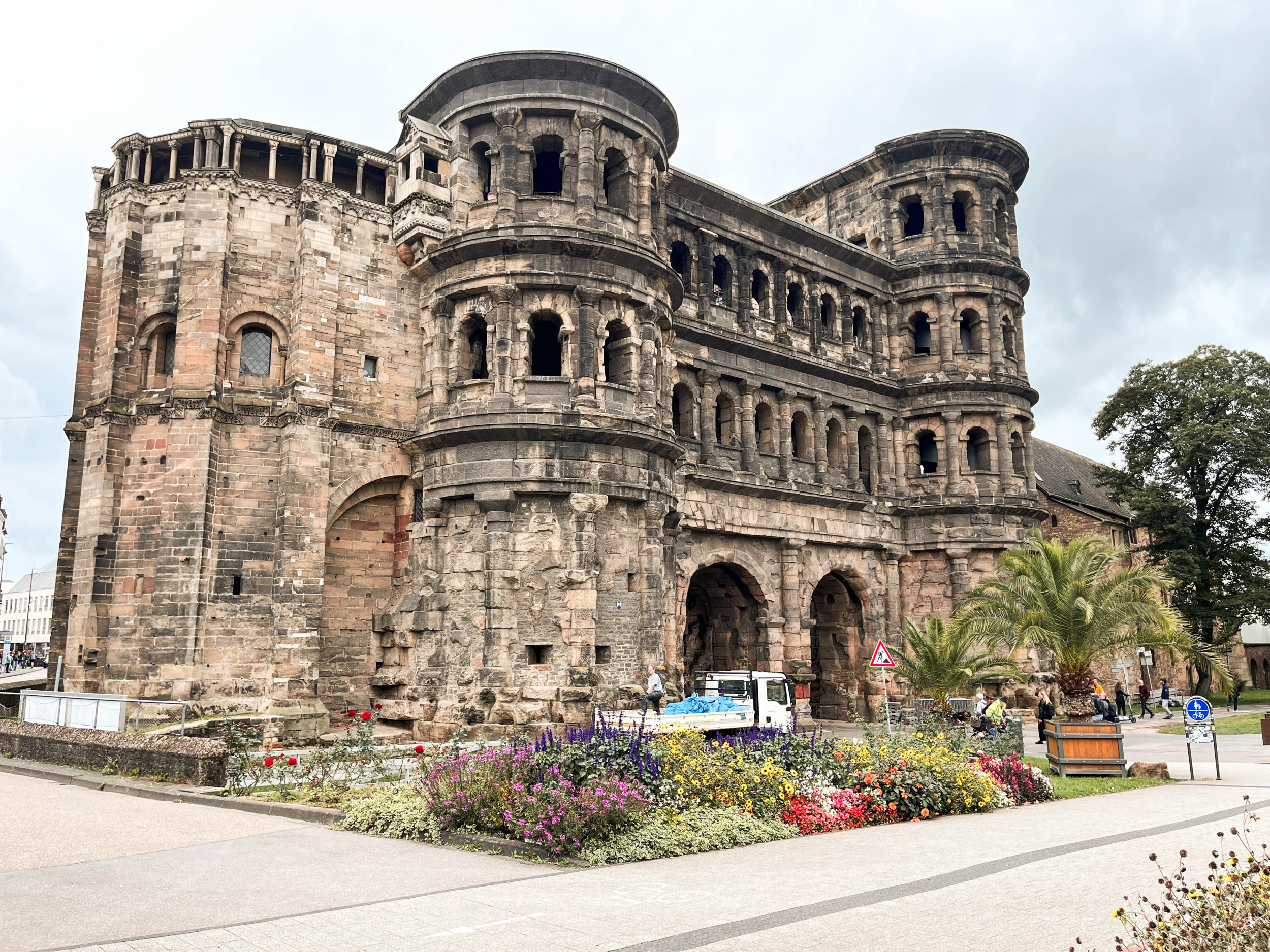 Kolossaal poortgebouw met twee poorten; ervoor een border met bloemen.