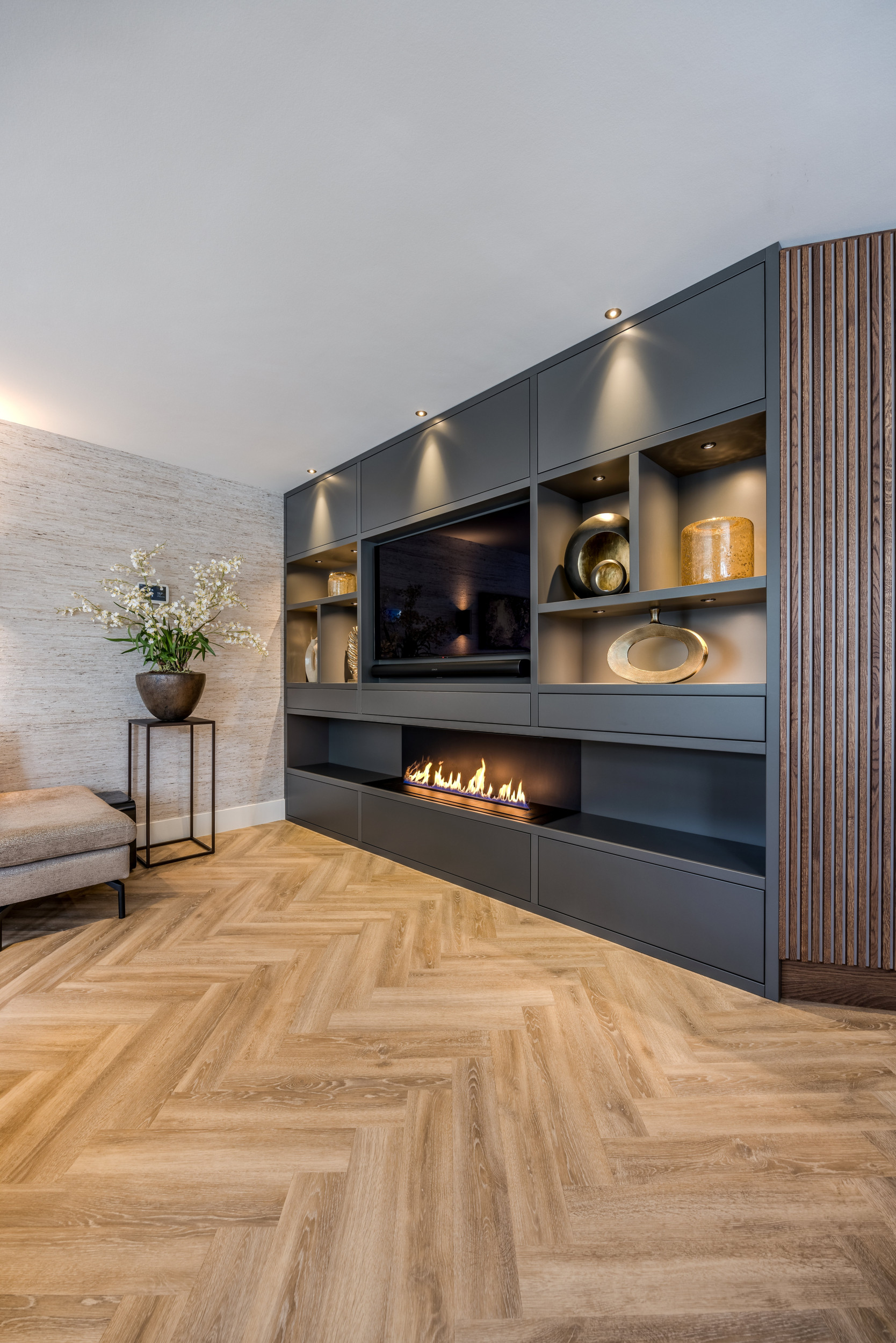 Hoek van een sfeervolle woonkamer met een donkere wandkast, gevuld met kunst, verlichting en een sfeerhaard