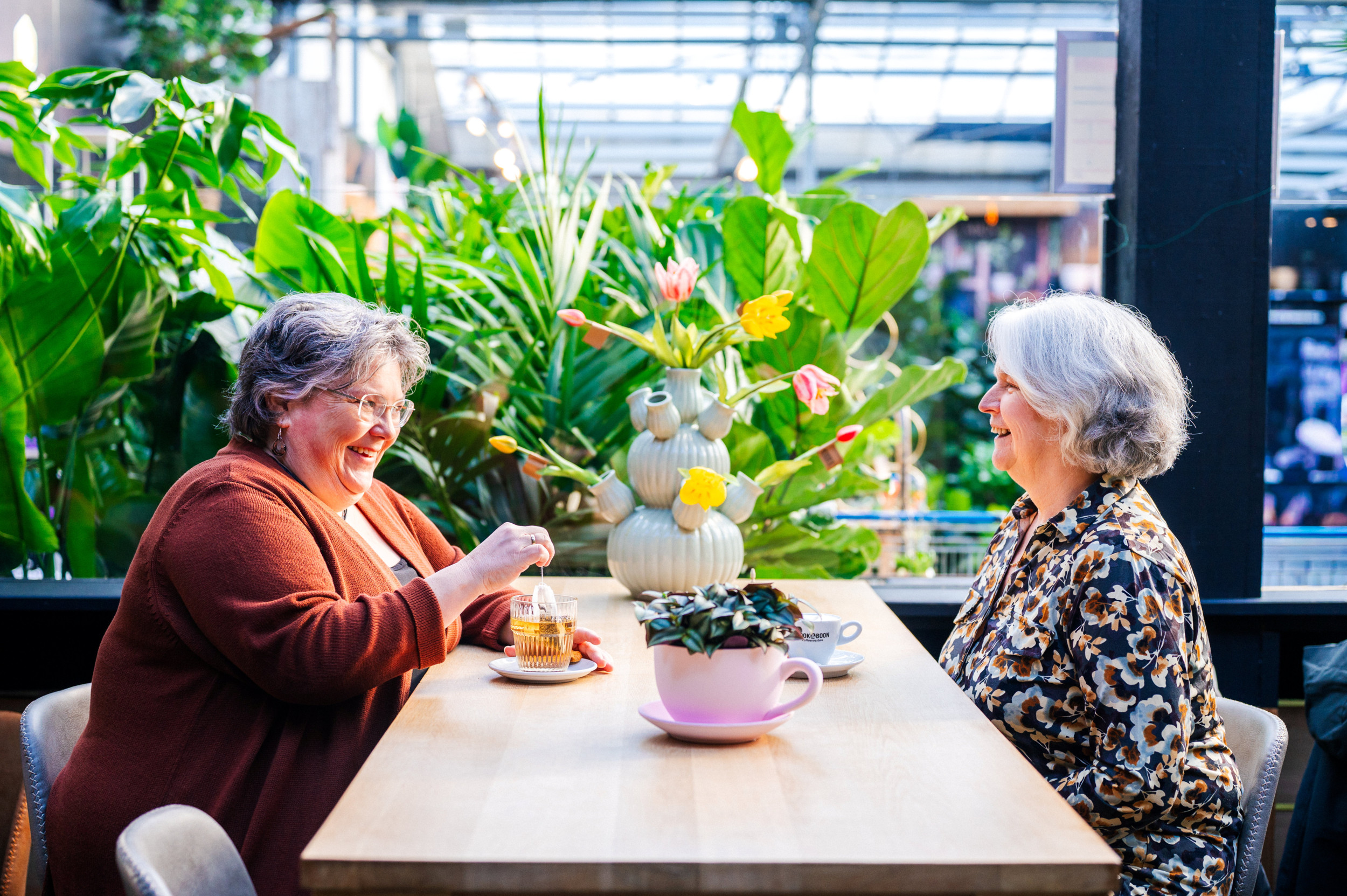 Twee vrouwen van middelbare leeftijd zitten aan een tafel, met koffie en thee.