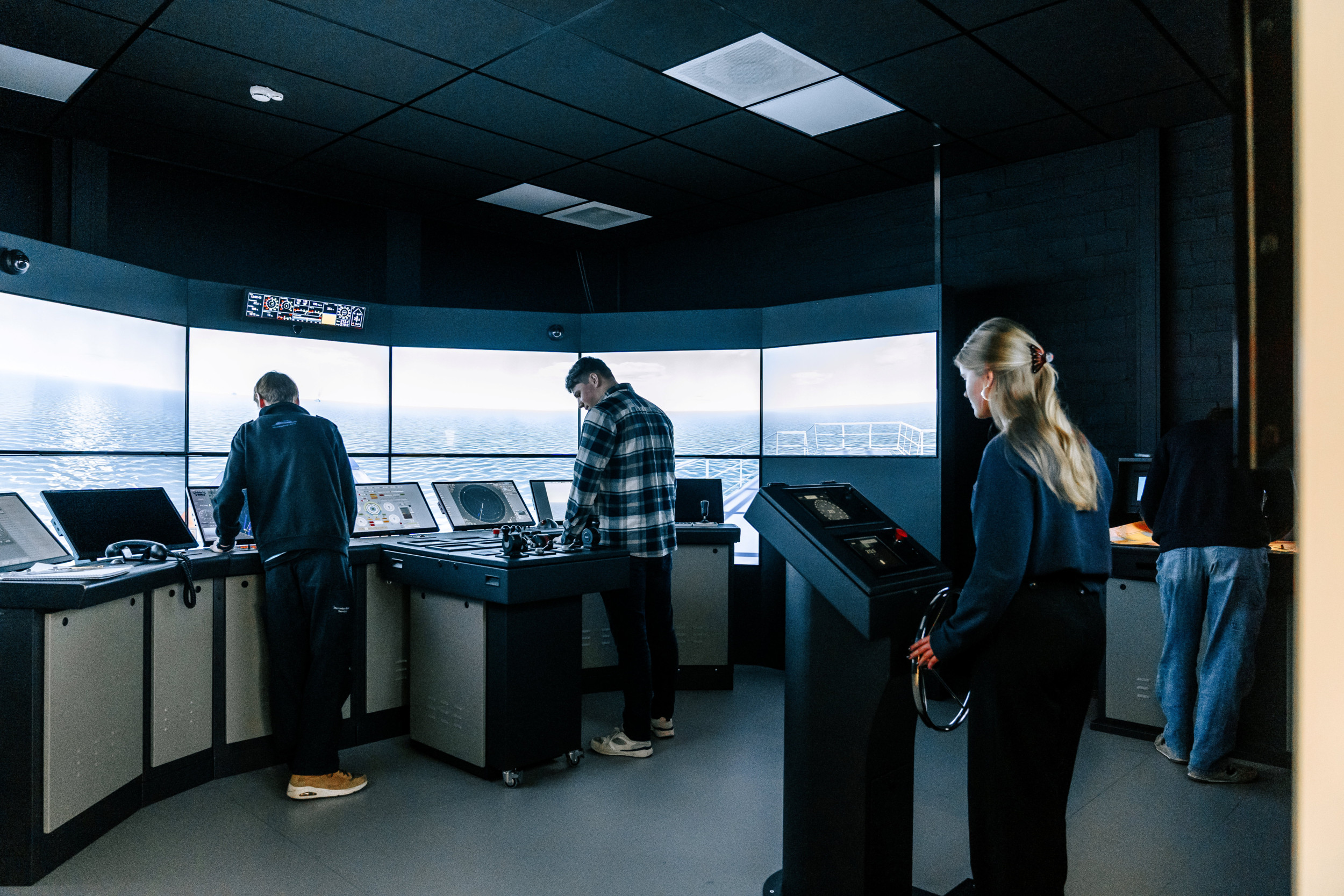 Drie jongens en een meisje in de simulator van de brug op een zeeschip.