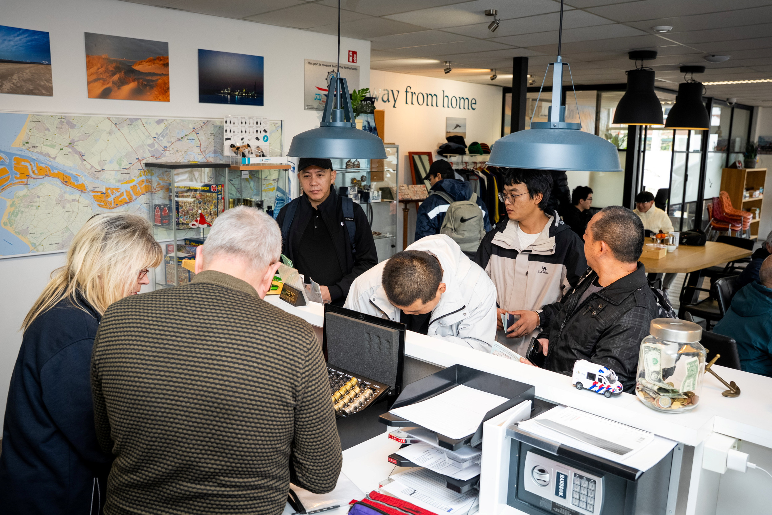 Zaal met buitenlandse mensen, achter de balie een Nederlandse man en vrouw.