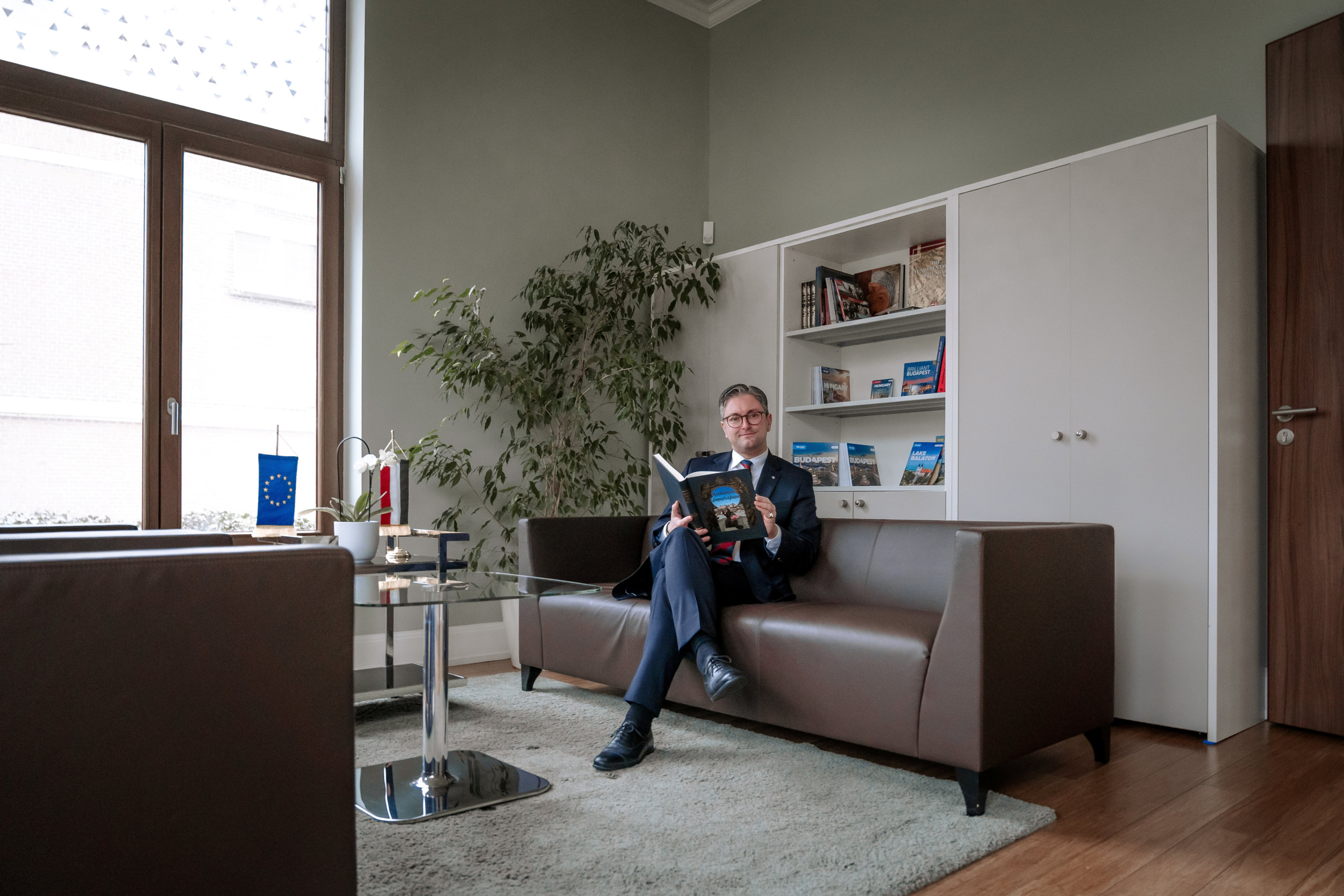 Man in donkerblauw pak, zittend op een bruine bank.