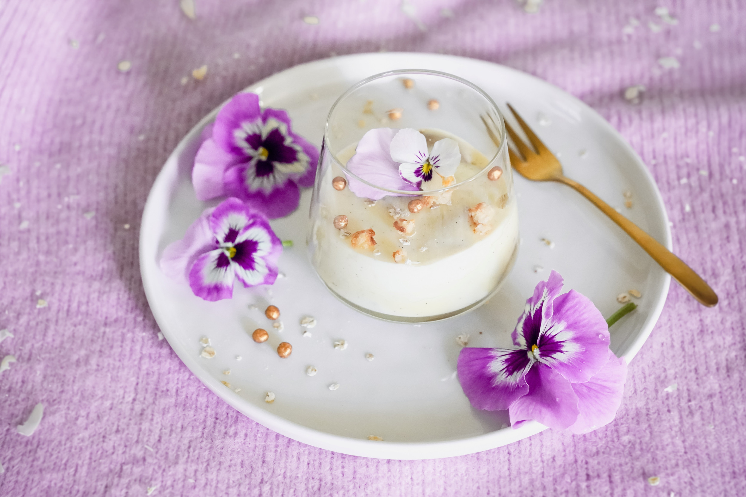 Glas met een toetje op een schotel met roze bloemblaadjes.