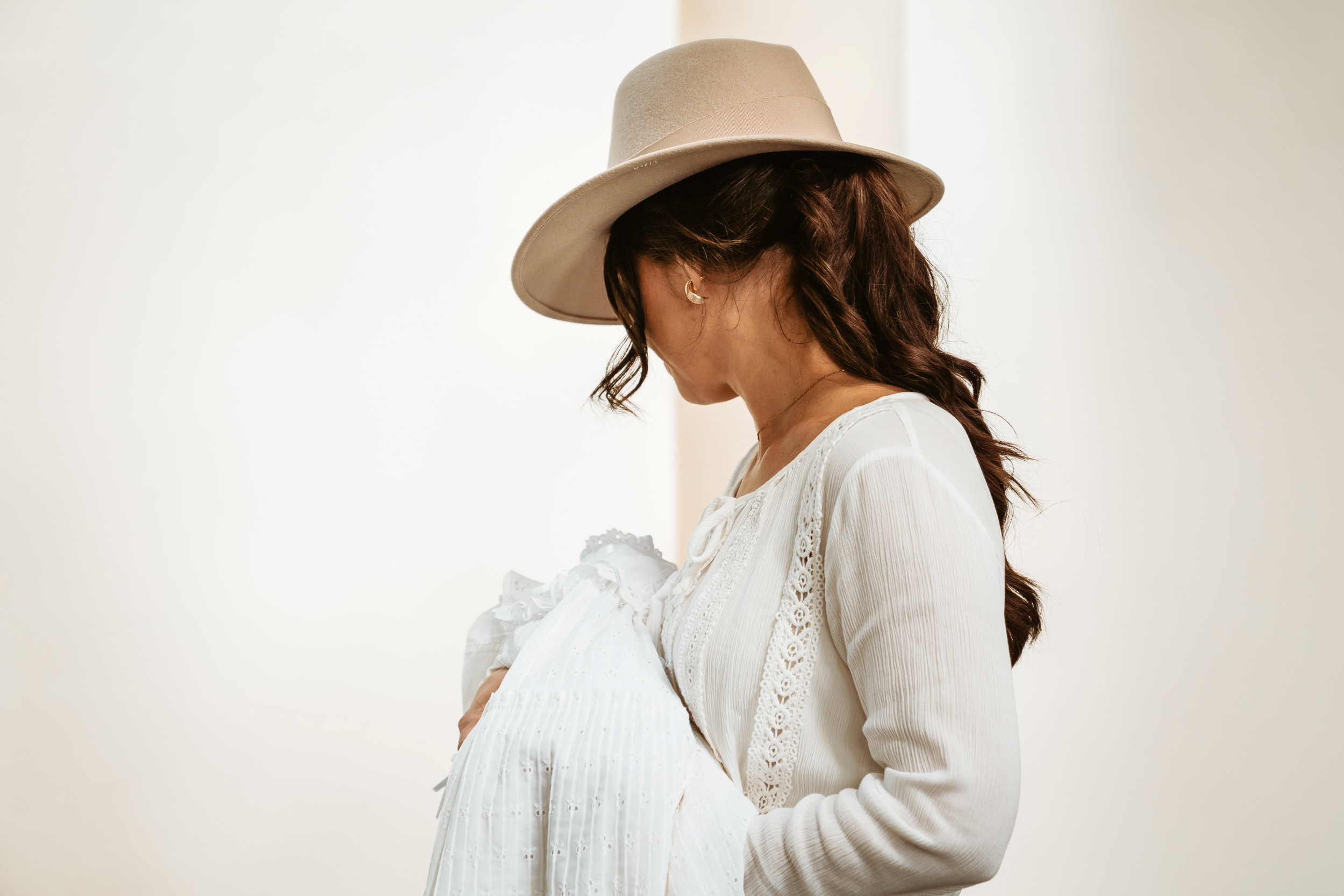 In het wit geklede vrouw met een beige hoed en een baby in de armen.