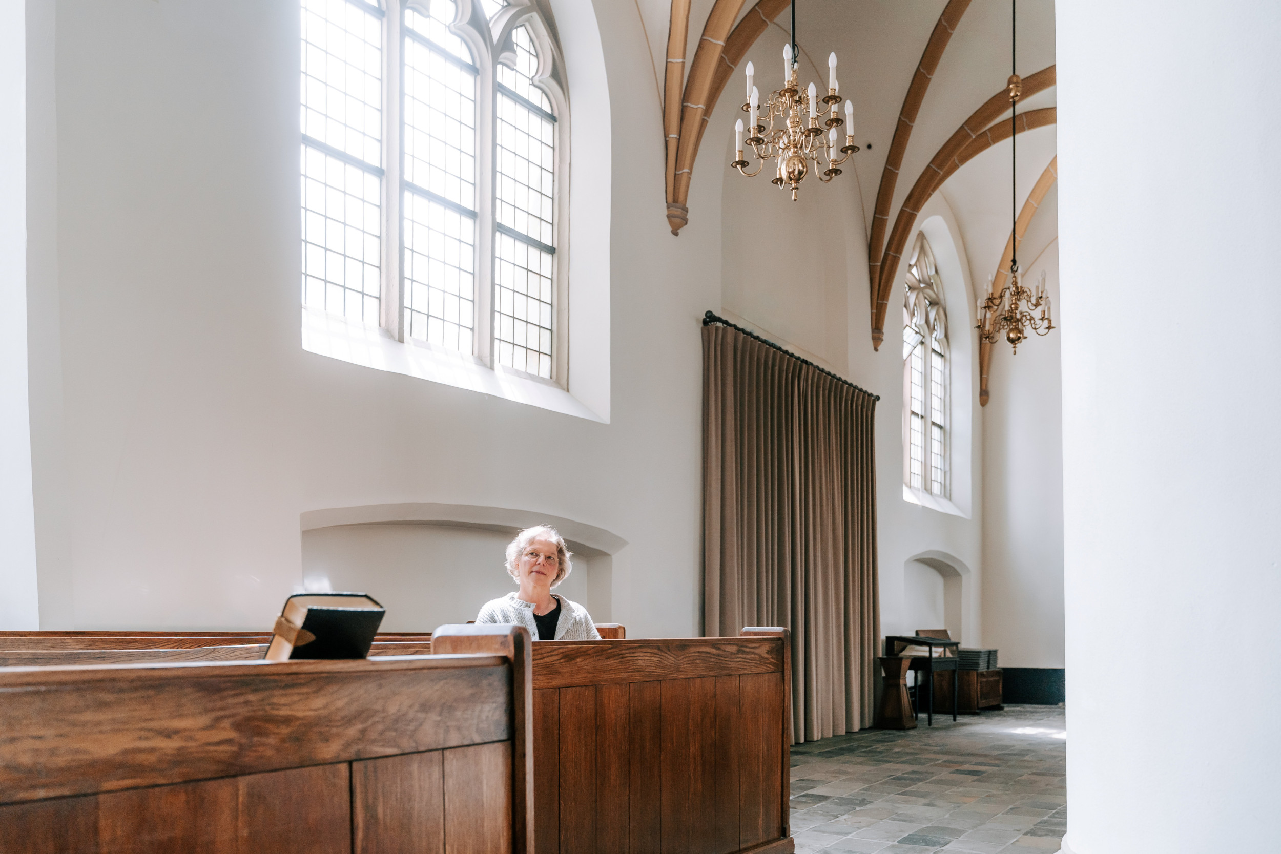 Vrouw van middelbare leeftijd, zittend in een kerkbank.