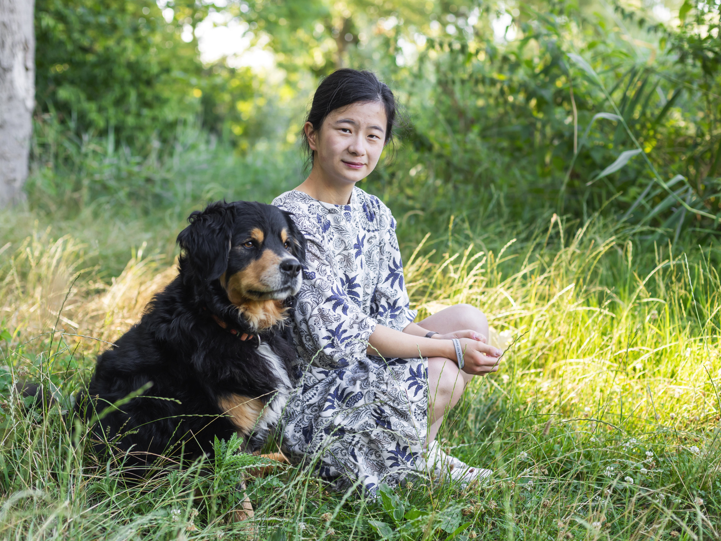 Vrouw met zwart haar en blauw-witte jurk, zittend naast een zwarte hond op het gras. Beeld Willemiene Smits.