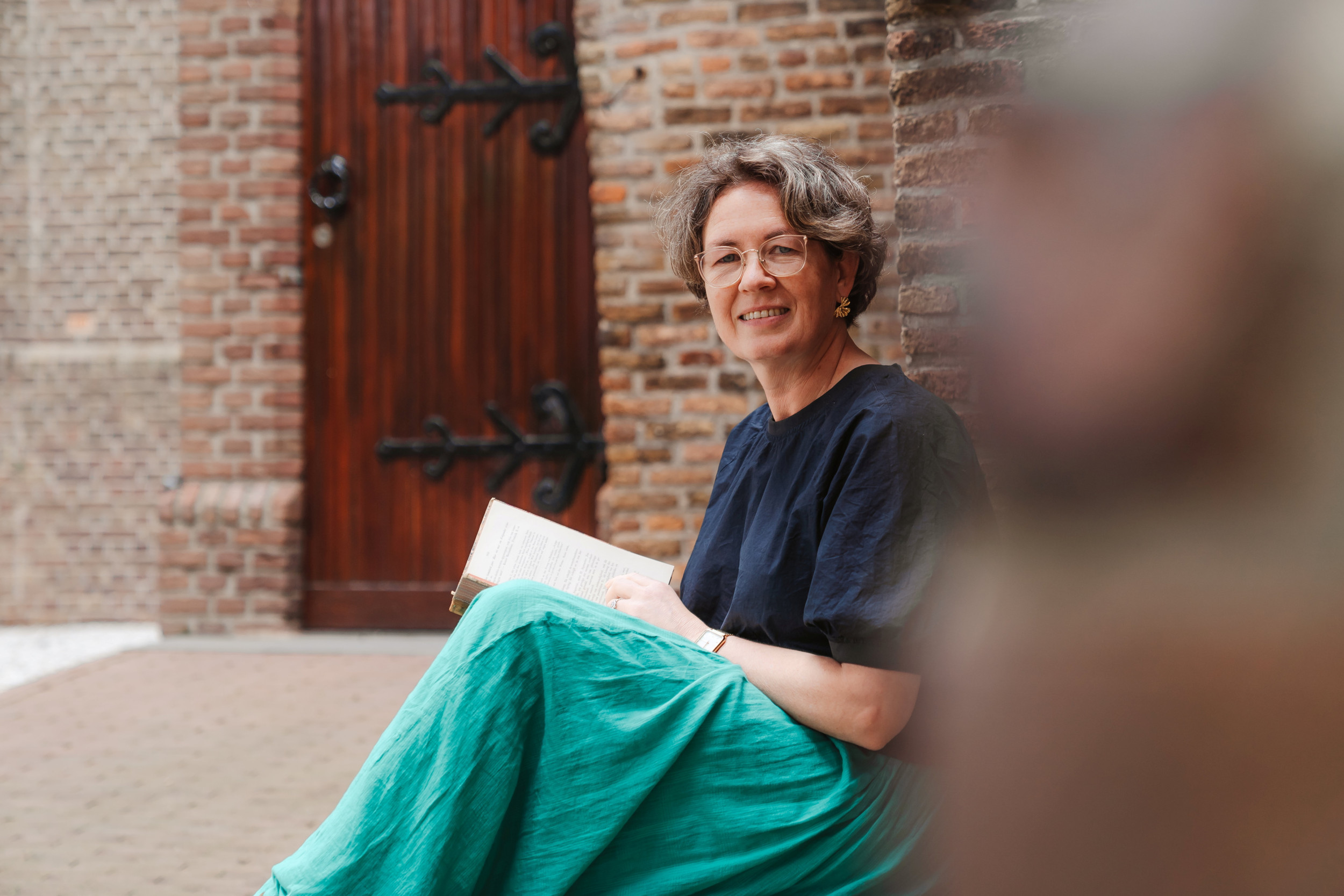 Vrouw met groene rok en blauw shirt, zittend op een stoep voor een oude kerk.