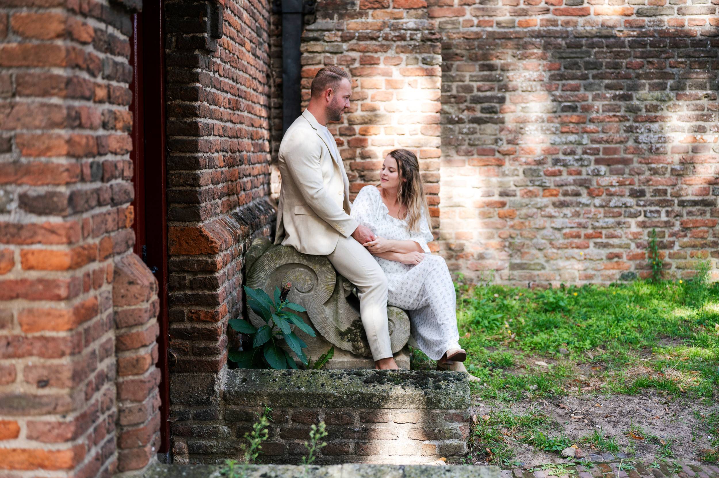 Jonge man en vrouw, zittend op een stenen bank tegen de muur van een kerk.