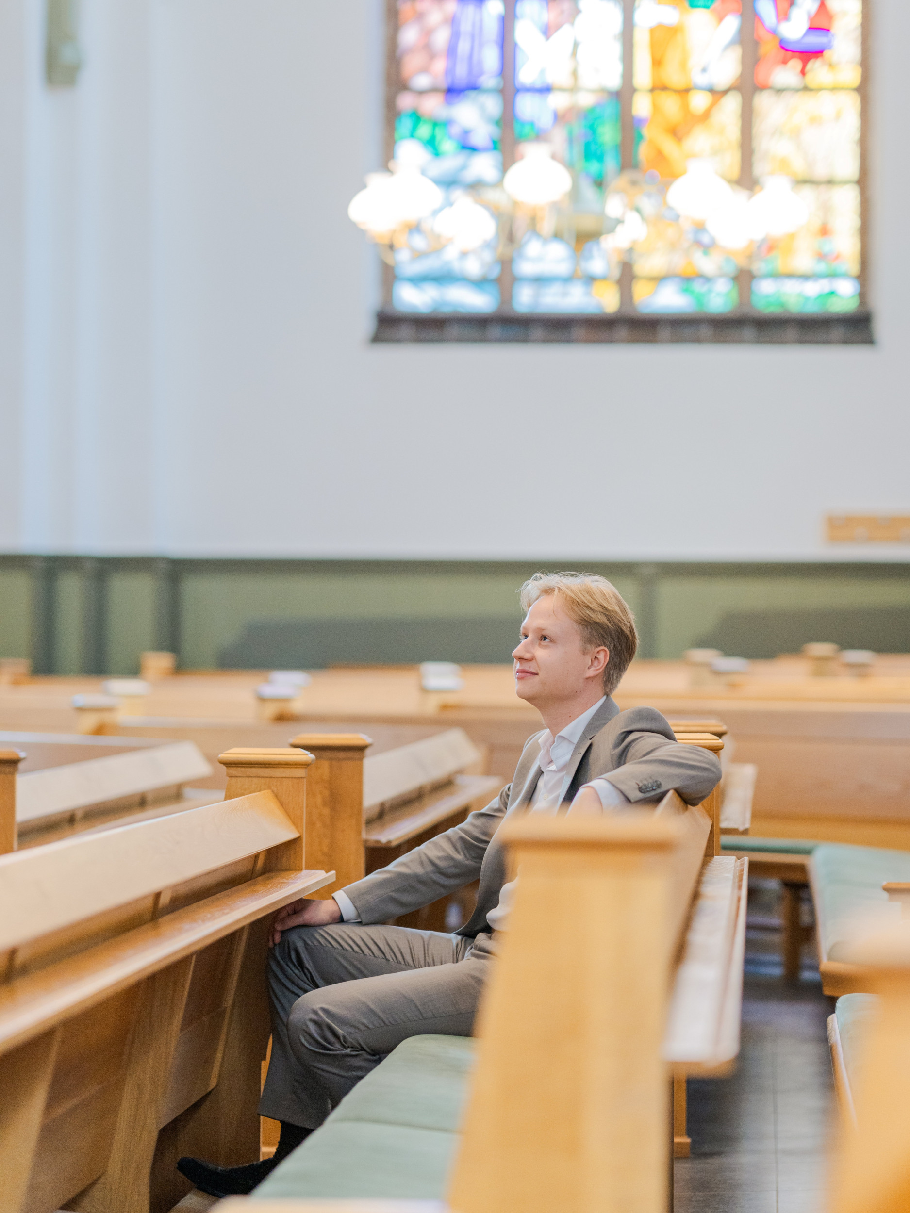 Jongeman met blond haar, gekleed in een licht pak, zittend in een kerkbank.