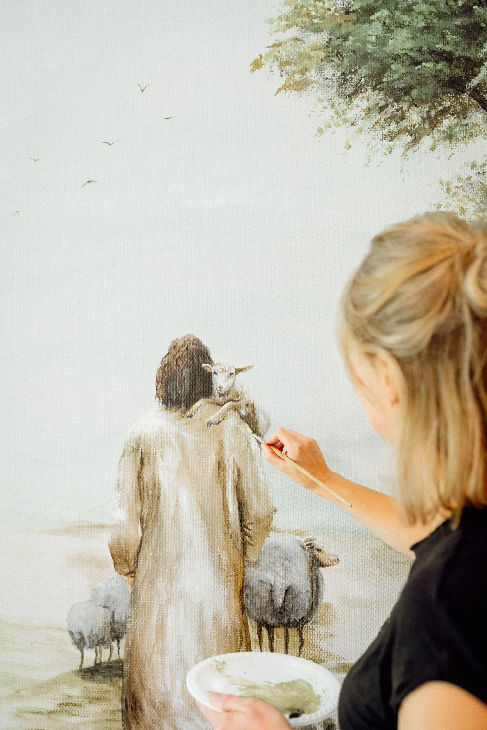 Een vrouw schildert op een muur een herder met een lam op de schouder.